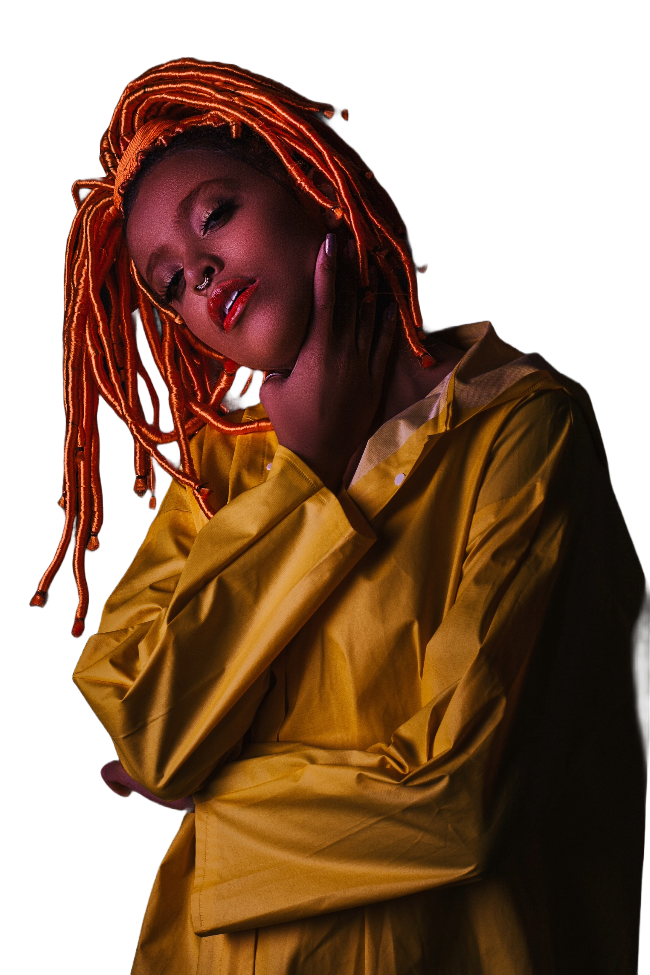 MyaDidIt studio portrait - a woman with orange locs in a yellow jacket, lit against a dark background.